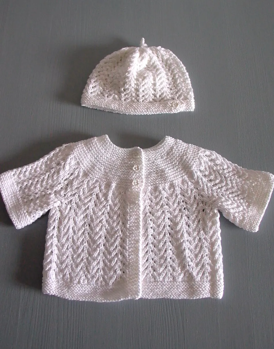 White knitted baby cardigan and matching hat laid flat