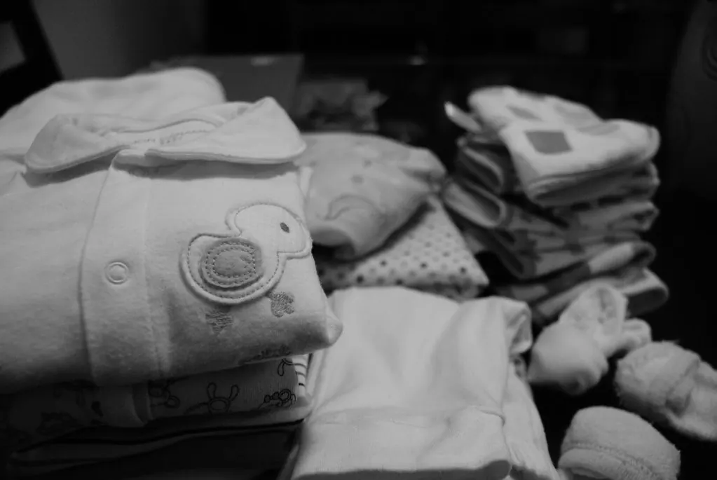 Folded baby clothes with a duck motif beside tiny socks