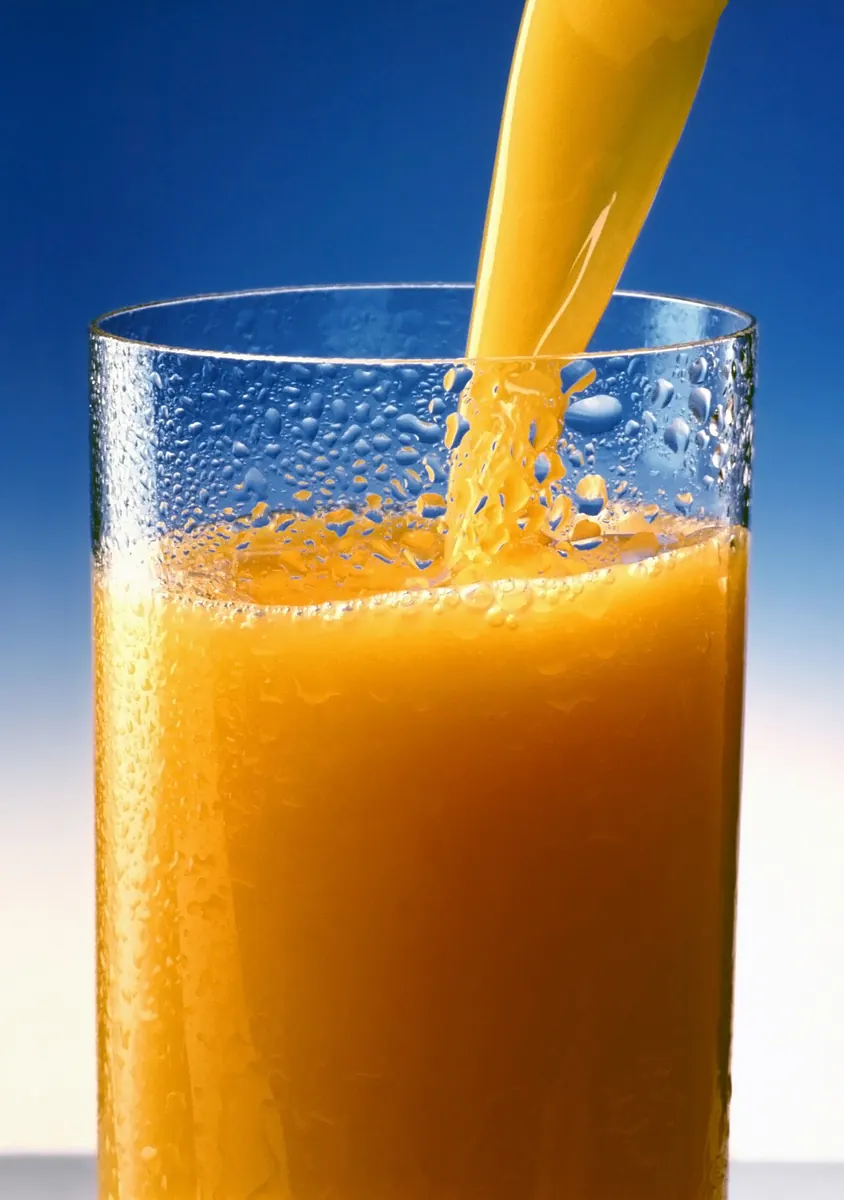 Orange juice being poured into a tall glass