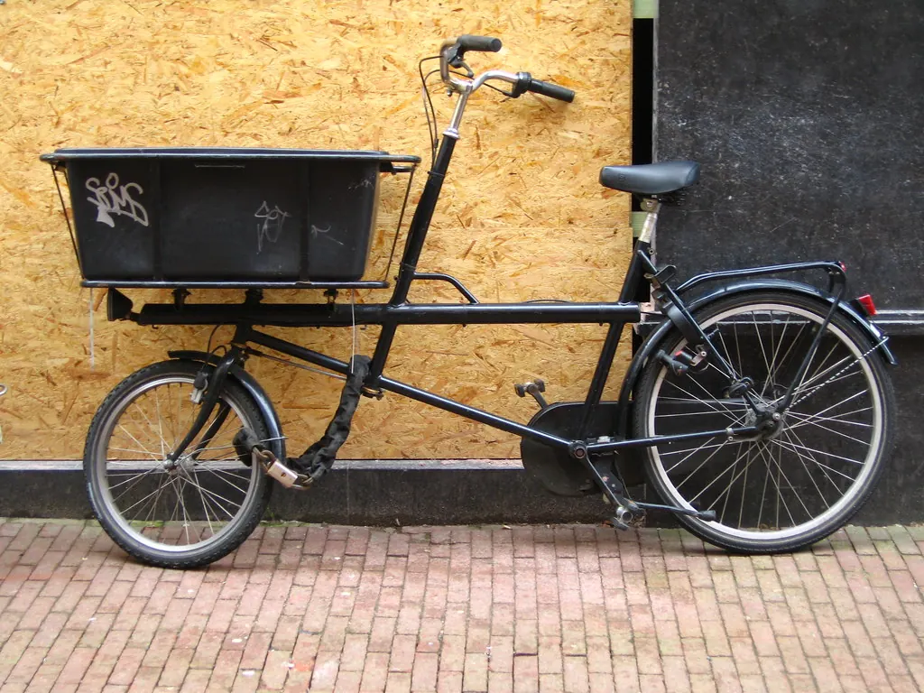 Black cargo bicycle with a front box parked on brick paving