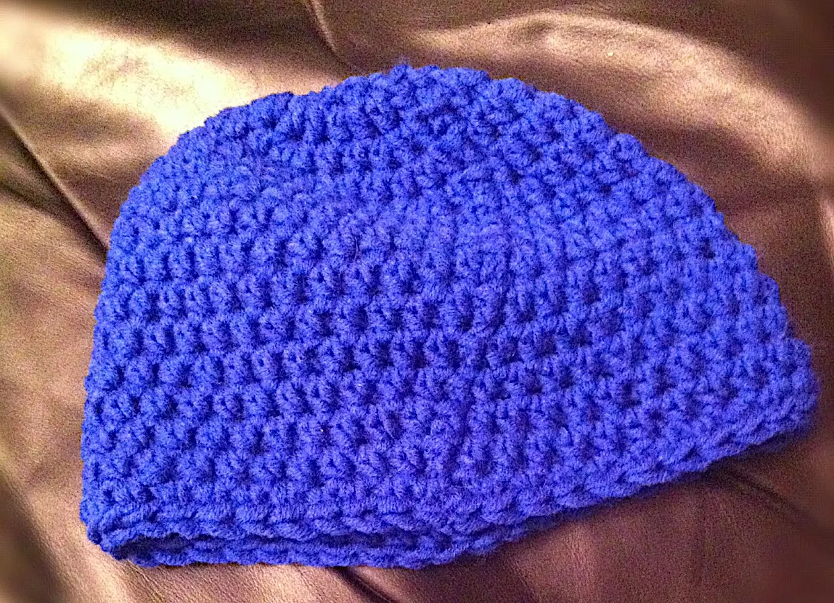 Blue crocheted beanie on a brown satin cloth