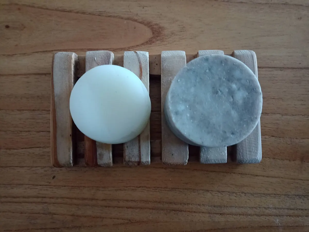 Two solid shampoo and conditioner bars on a wooden rack