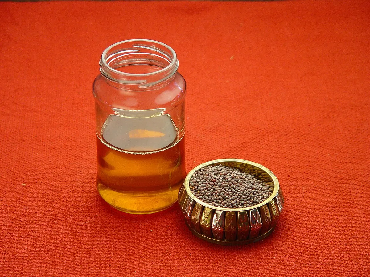 Jar of mustard oil beside a bowl of mustard seeds