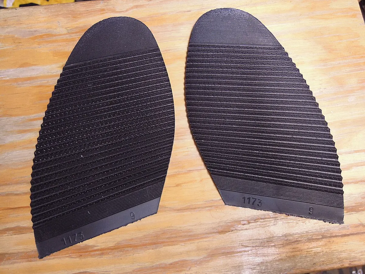 Two black ribbed rubber half soles on a wooden table