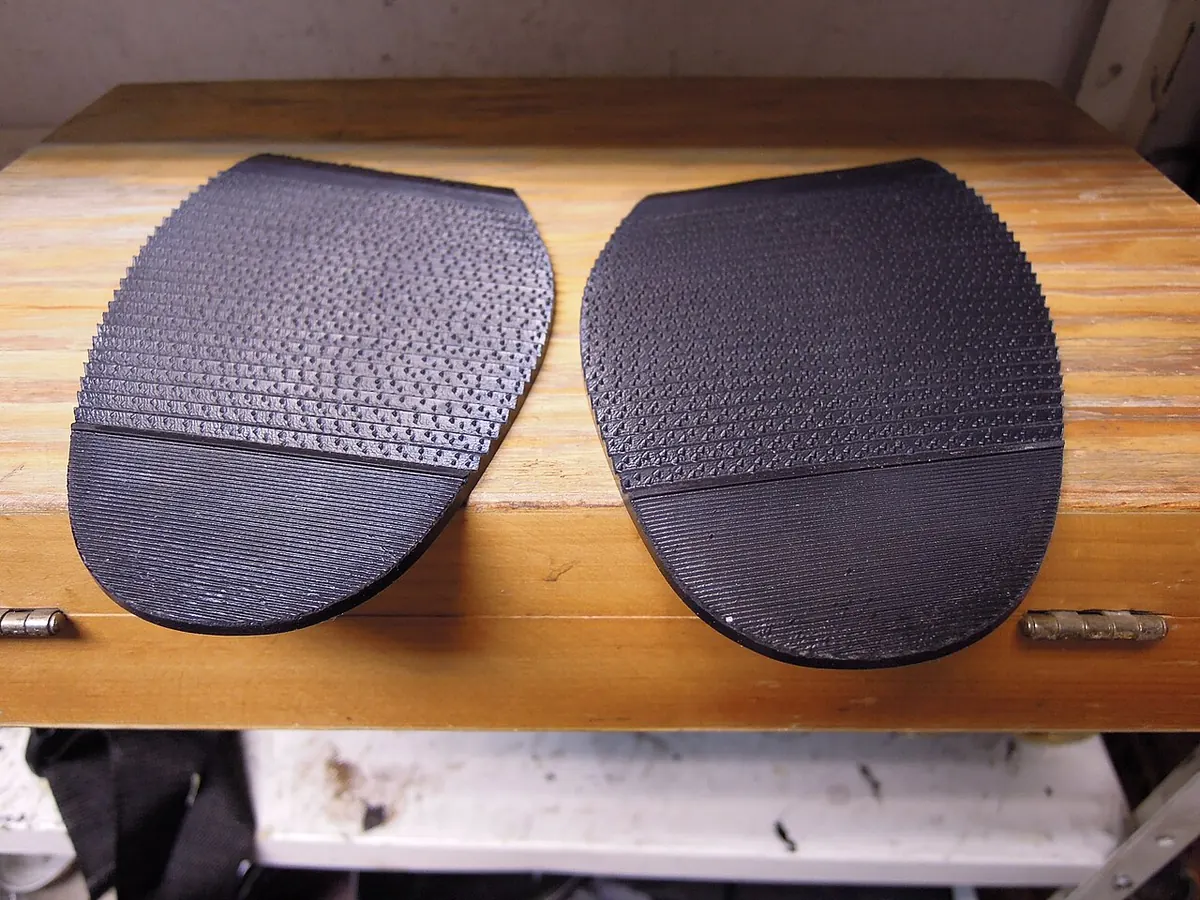 Two black rubber half soles with a textured tread on wood