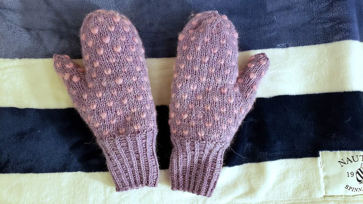 Pair of purple knitted mittens on a striped towel