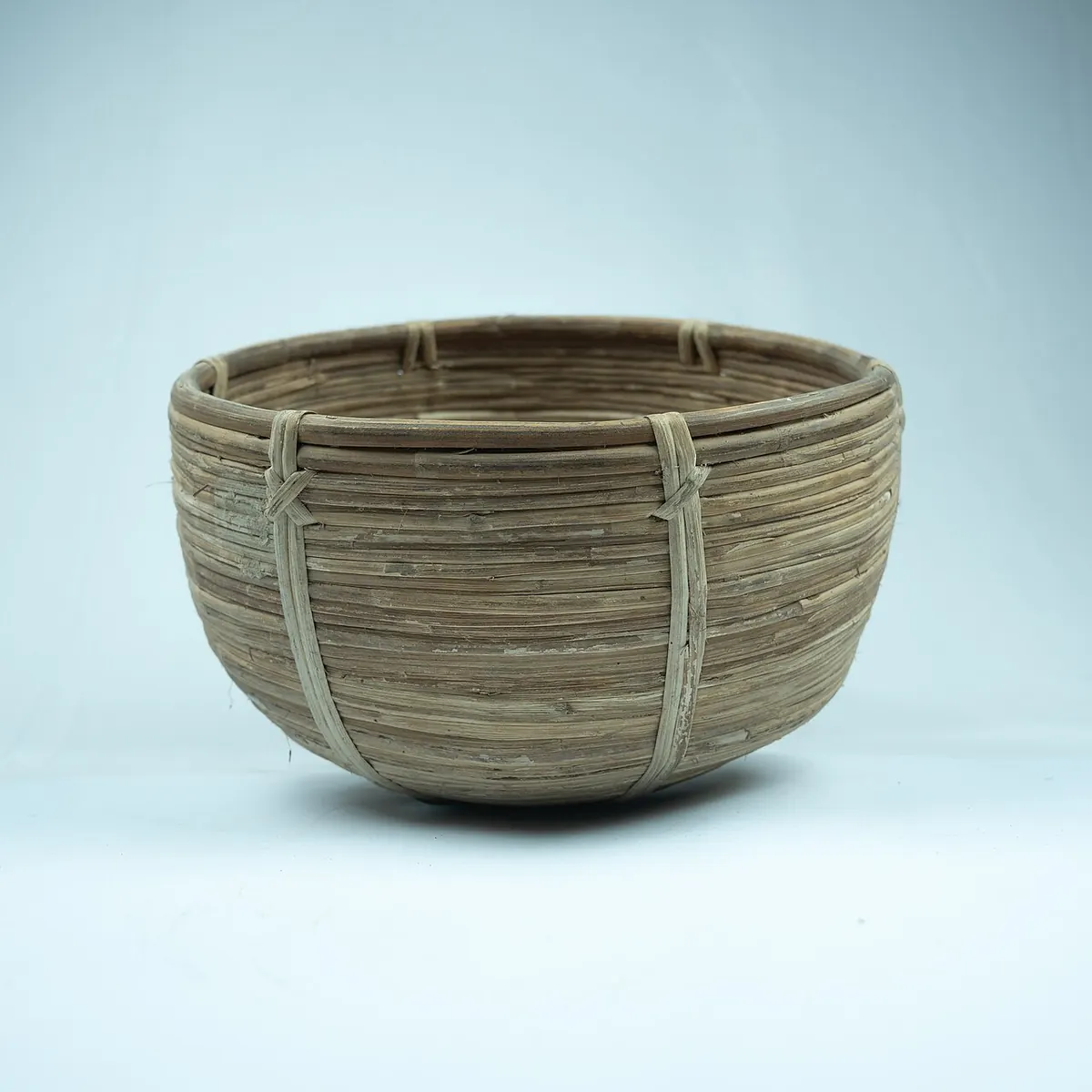 Round rattan basket with cane bindings on a pale blue background
