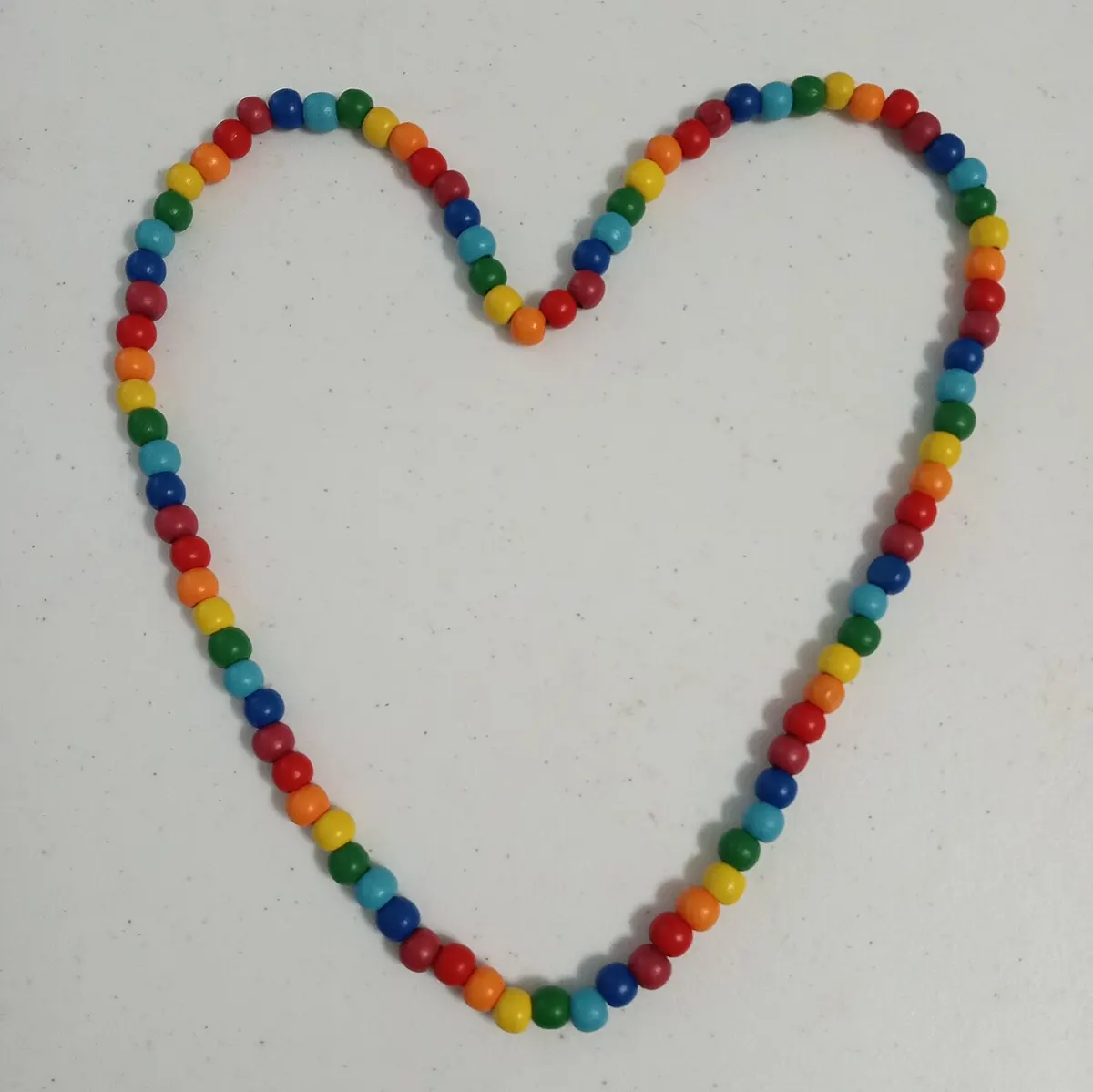 Rainbow painted wooden bead necklace laid in a heart shape