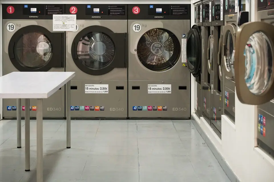 A row of large industrial washing machines in a laundromat, each labeled with numbers and 