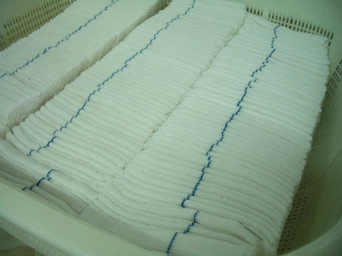 Stacks of folded surgical gauze swabs in a plastic crate