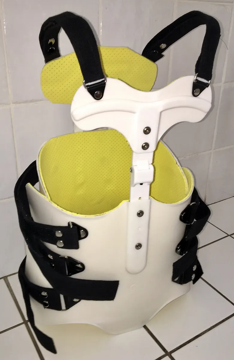 White plastic back brace with black straps on a tiled floor