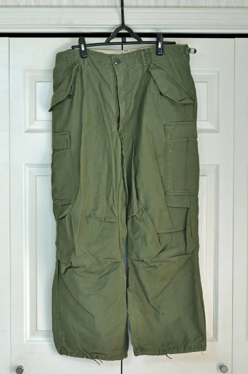 Olive cargo trousers on a hanger against a white door