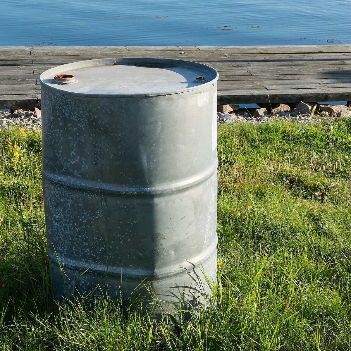 Plain steel oil drum standing on grass by the water