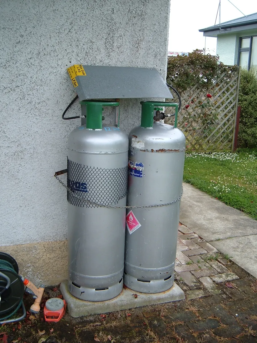 Two grey LPG cylinders standing against a house wall