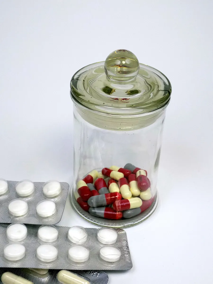 Glass jar of capsules beside blister packs of white tablets