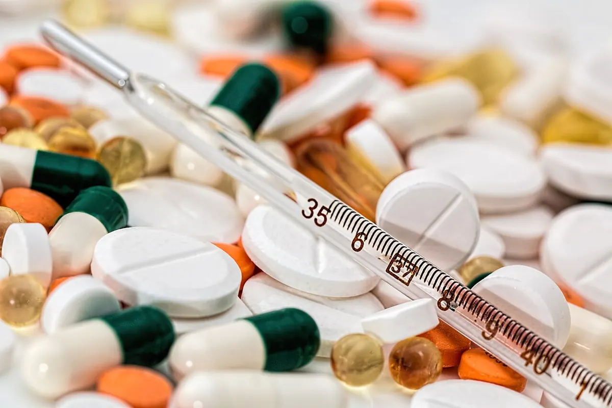 Pile of tablets and capsules with a glass thermometer