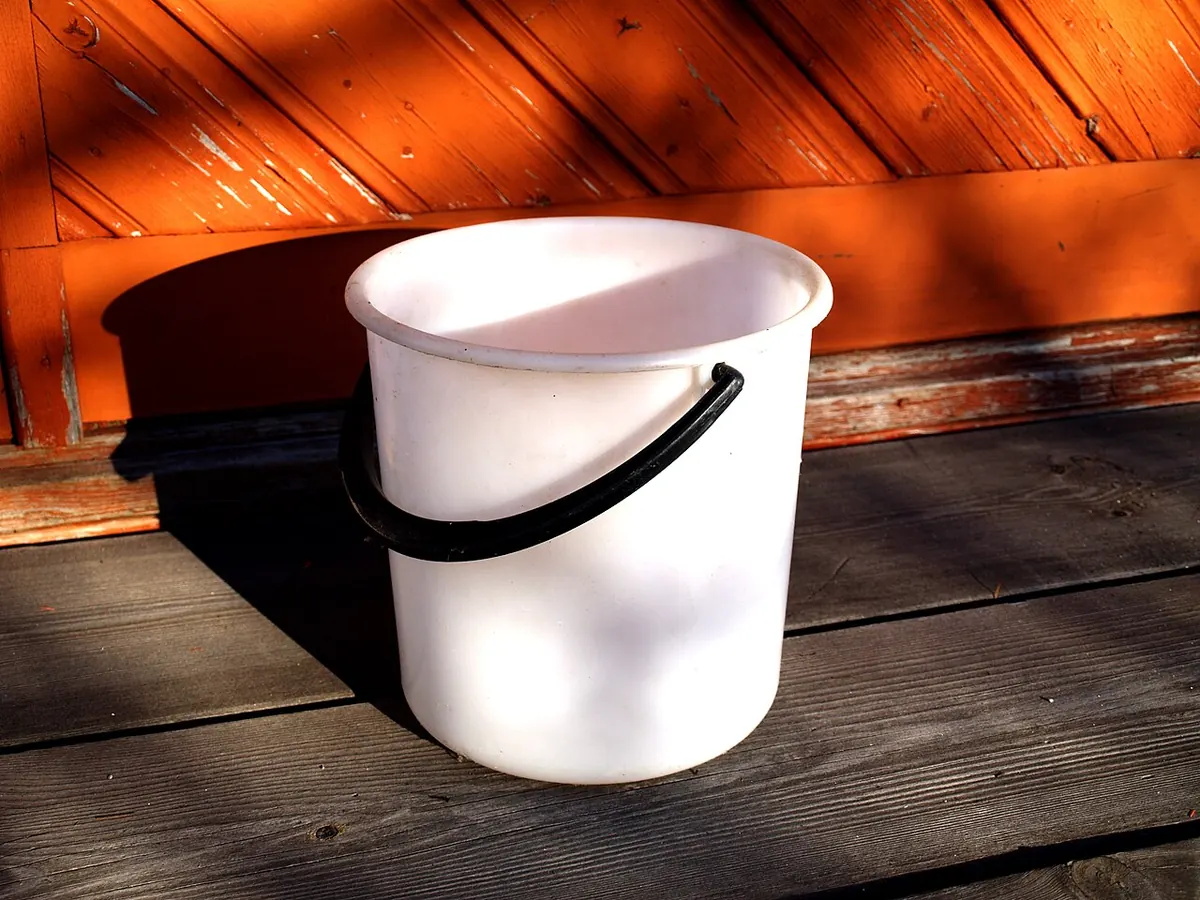 White plastic bucket with a black handle on a wooden deck