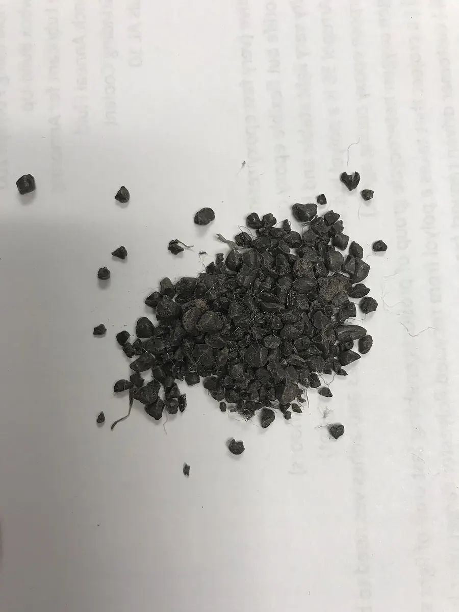 Small heap of dark recycled PET granules on paper
