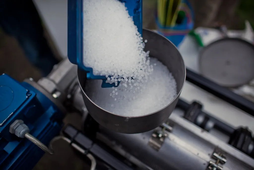 White plastic pellets poured from a scoop into a machine hopper