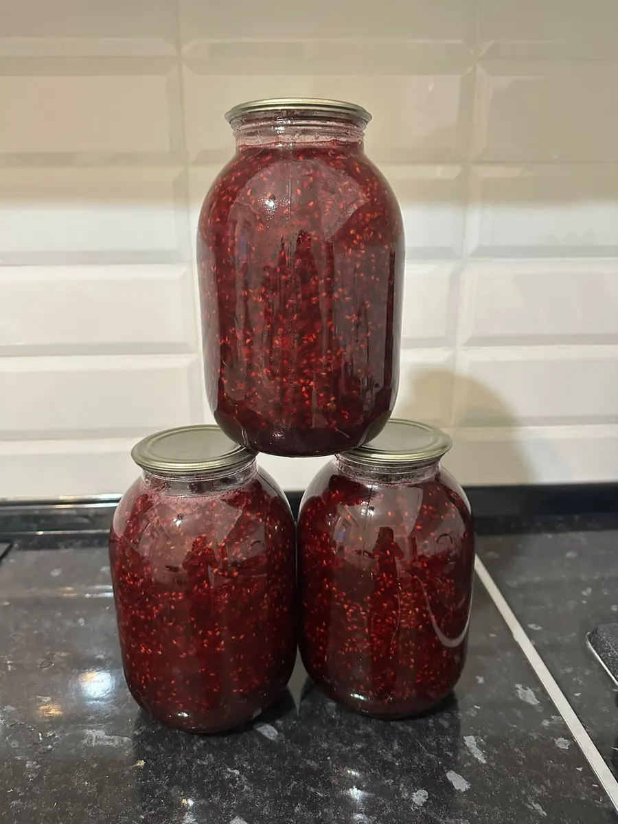 Three glass jars of red berry jam stacked on a counter