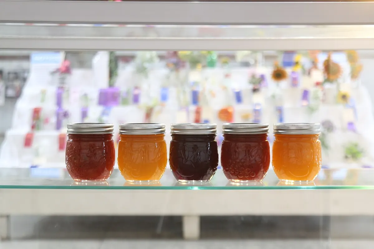 Five jars of fruit preserves on a glass shelf