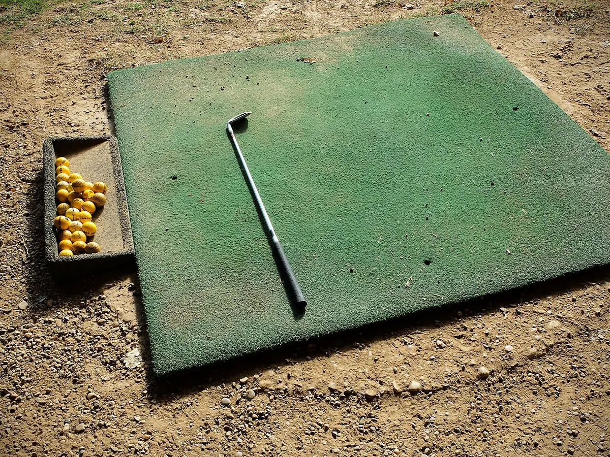 Golf club and a tray of practice balls on a hitting mat