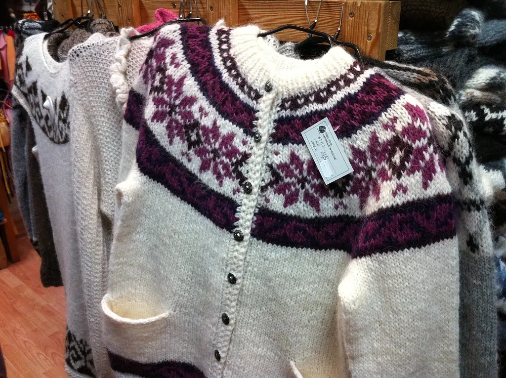 Cream wool cardigan with a purple patterned yoke on a hanger
