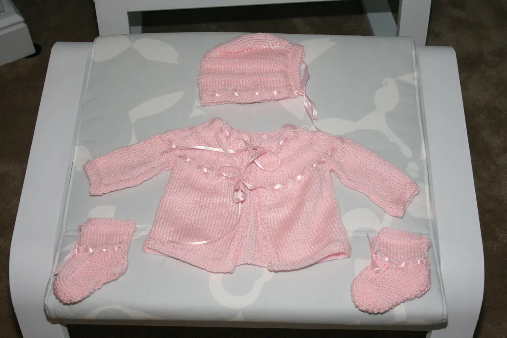 Pink knitted baby cardigan with matching bonnet and booties