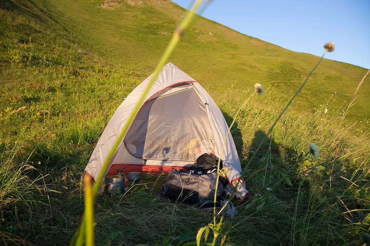 Small dome tent pitched on a grassy mountain ridge