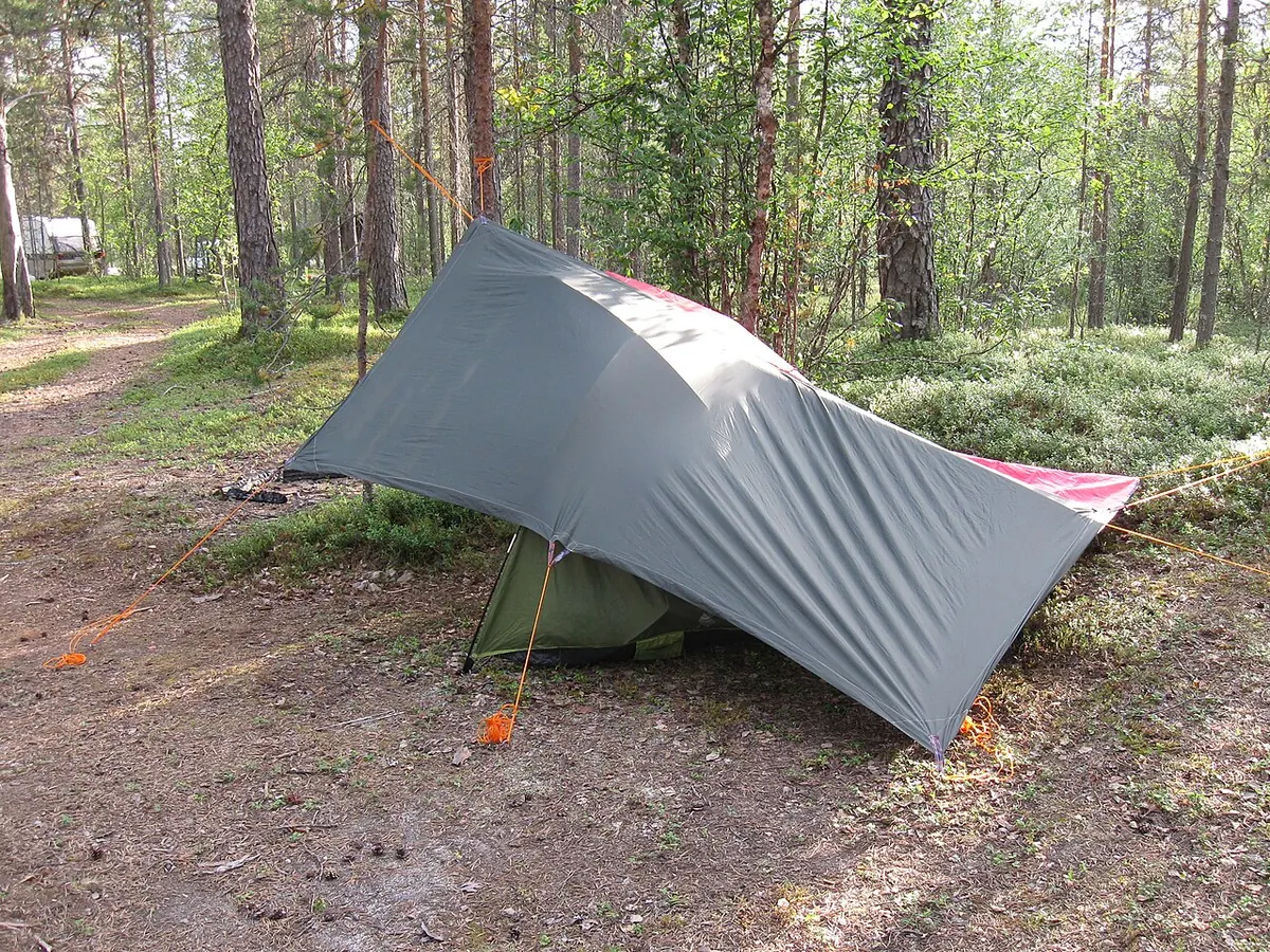 Grey tarpaulin pitched over a small tent in a pine forest