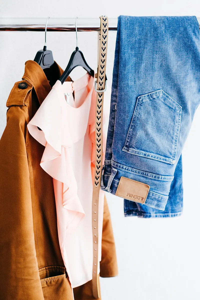 Pink ruffled blouse, tan jacket and jeans on a rail