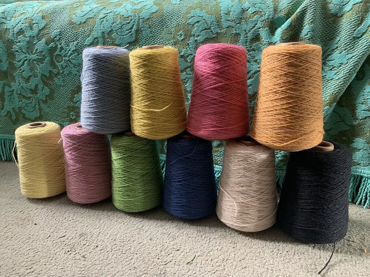 Row of coloured yarn cones on a lace cloth